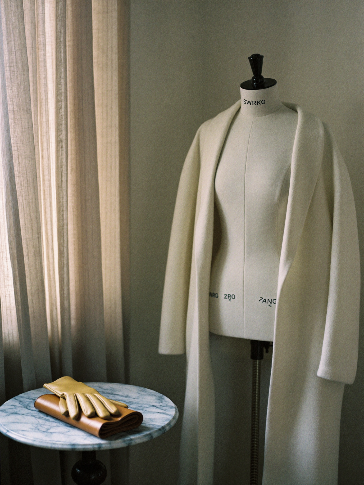 Styling-Atelier mit ivory-farbenem Wollmantel auf einer Schneiderpuppe, Lederhandschuhen und weichem Nordlicht.